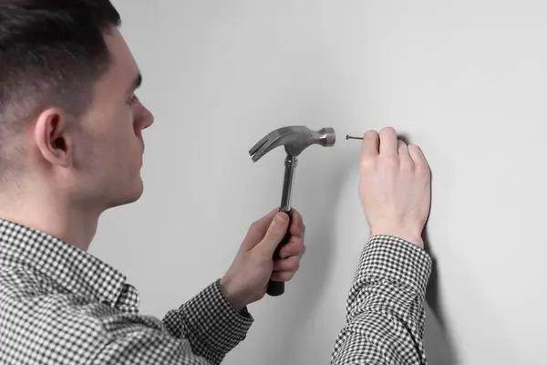 Young Man Hammering Nail White Wall Indoors — Stock Photo, Image