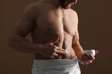 Kahverengi arka planda vücuduna nemlendirici krem süren bir adam.