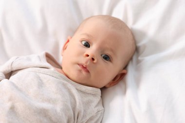 Beyaz çarşafların üzerinde uzanmış şirin bir bebek.