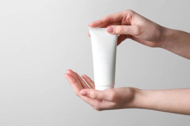 Gri arka planda bir krem tüpü tutan kadın, yakın plan. Metin için boşluk