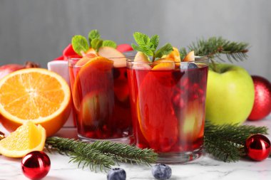 Aromatik Sangria içeceği bardaklarda, malzemelerde ve beyaz mermer masada Noel dekorunda.