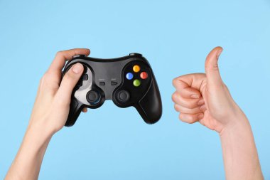 Oyun denetleyicisi olan kadın açık mavi arkaplanda başparmak gösteriyor, yakın plan