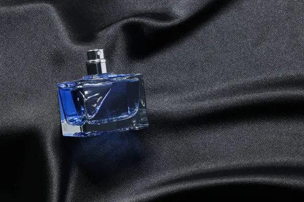 Luxury men\'s perfume in bottle on black satin fabric, top view. Space for text