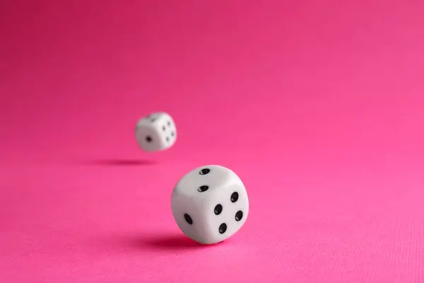 Two white game dices falling on pink background, closeup. Space for text