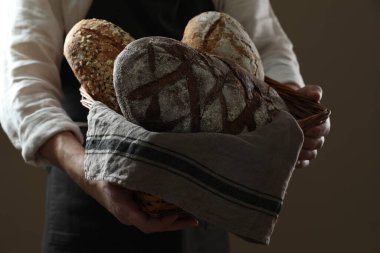 Hasır sepeti tutan adam kahverengi arka planda farklı ekmek türleri, yakın plan