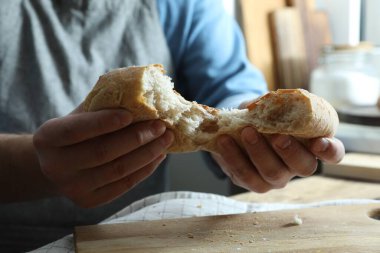 İçerideki ahşap masada ekmek kıran adam, yakın plan.