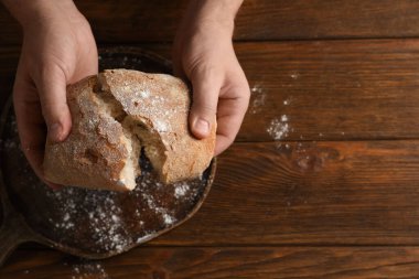Ahşap masada taze ekmek kıran bir adam, üst manzara. Metin için boşluk