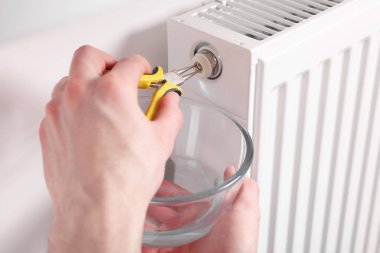 Profesyonel tamirci içeride penseyle ısıtma radyatörünü tamir ediyor.