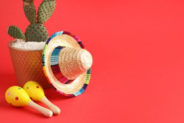 Kırmızı arka planda Meksika şapkası, kaktüs ve marakas. Metin için boşluk