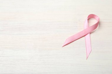 Açık ahşap masada pembe farkındalık kurdelesi, manzaranın üstünde. Metin için boşluk