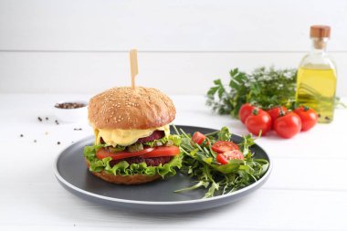 Beyaz ahşap masada salata ile servis edilen lezzetli vejetaryen burger.