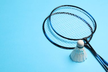 Tüy badminton mekik horozları ve raketler açık mavi arkaplan, metin için boşluk