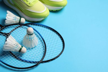 Tüy badminton mekik, raket ve spor ayakkabıları açık mavi arka planda, metin için boşluk