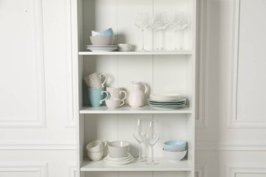 Dolabın içindeki raflarda farklı temiz bulaşık malzemeleri ve bardaklar var.