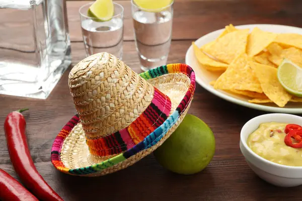 Mexican sombrero hat, tequila with lime, chili peppers, nachos chips and dip sauce on wooden table