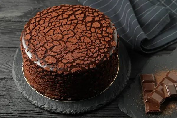 Delicious truffle cake and chocolate pieces on black wooden table
