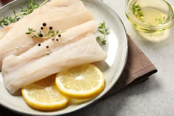 stock image Plate with raw cod fish, spices, microgreens and lemon on grey table, closeup