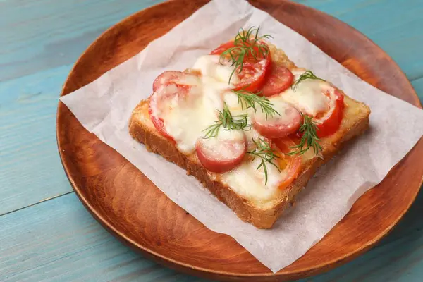 Tasty pizza toast with cheese, tomato and dill on light blue wooden table, closeup