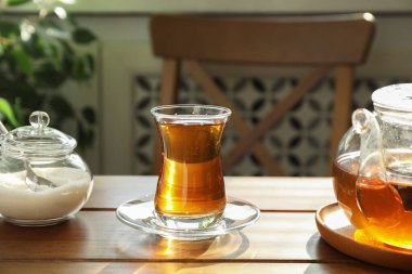 Bardakta Aromatik çay, içeride ahşap masada çaydanlık ve şeker