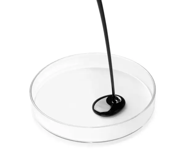 stock image Pouring black crude oil into Petri dish on white background