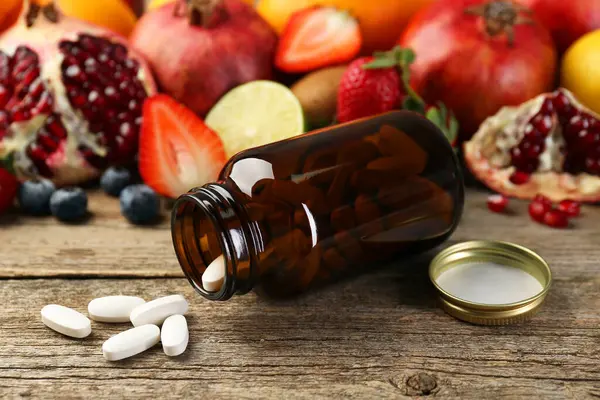 Vitamin hapları, şişe ve ahşap masada taze meyve.