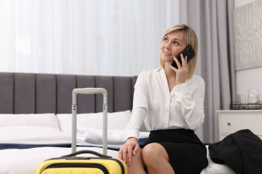 Gülümseyen iş kadını şık bir otel odasında akıllı telefondan konuşuyor.