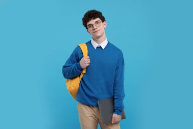 Açık mavi arkaplanda sırt çantası ve dizüstü bilgisayarı olan öğrencinin portresi