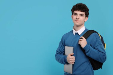 Açık mavi arka planda sırt çantası ve dizüstü bilgisayarı olan öğrencinin portresi. Metin için boşluk