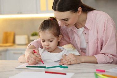 Anne ve küçük kızı mutfaktaki masada renkli kalemlerle resim çiziyorlar.