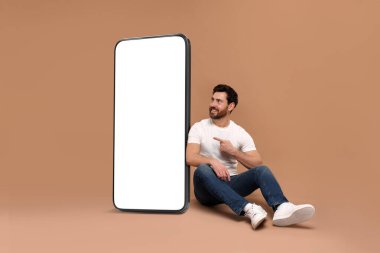 Koyu bej arka planda boş ekranı olan büyük bir cep telefonunun yanında oturan adam. Tasarım için model