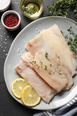 Çiğ morina balığı, mikro yeşillik, baharat ve limon tabağı koyu masada, düz yerde.