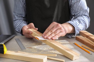 Gri masadaki zımpara kağıdıyla tahta cilalayan adam, yakın plan.