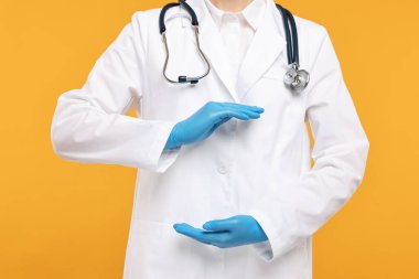 Steteskoplu doktor turuncu arka planda bir şey tutuyor, yakın plan.