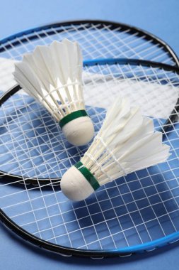 Tüylü badminton mekikleri ve raketleri mavi arka planda yakın plan