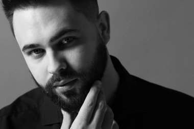 Gri arka planda sakallı yakışıklı bir adamın portresi. Siyah ve beyaz etkisi