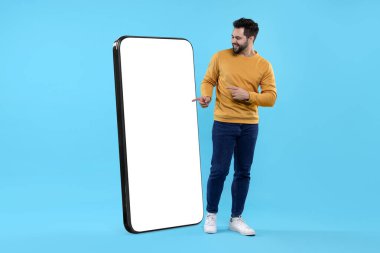 Adam açık mavi arka planda boş ekranı olan büyük bir cep telefonunu işaret ediyor. Tasarım için model