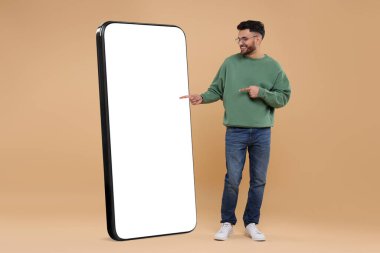Koyu bej arka planda boş ekranı olan büyük bir cep telefonunu işaret eden bir adam. Tasarım için model