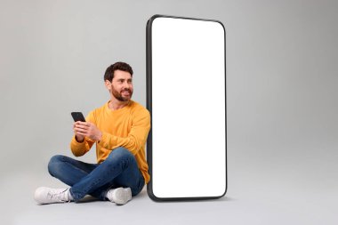 Cep telefonu olan bir adam gri arka planda boş ekranı olan büyük bir cihazın yanında oturuyor. Tasarım için model