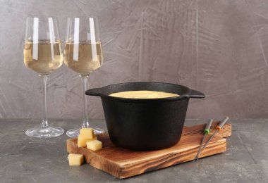 Lezzetli eritilmiş peynirli fondü tenceresi, çatal ve şarap gri masada.