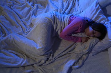 Genç bir kadın gece yumuşak bir yatakta uyuyor.