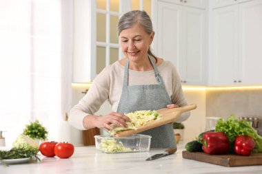 Mutlu ev hanımı, mutfaktaki beyaz mermer masada kesilmiş lahanayı cam kabın içine koyuyor.