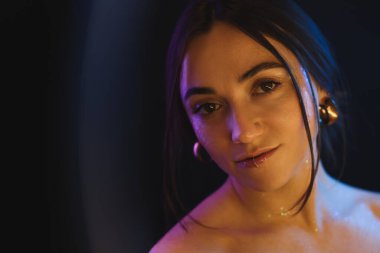 Koyu arkaplanda güzel bir kadının portresi neon ışıklarıyla, yüzük lambasının arkasından.
