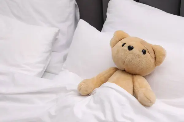 Toy cute bear with sticking plaster under blanket in bed