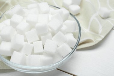 Beyaz ahşap masada cam kasede bir sürü şeker küpü, yakın plan.