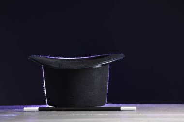 Sihirbaz şapkası ve değneği siyah arka plana karşı beyaz ahşap masada.