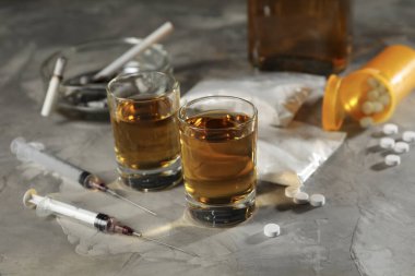 Alkol ve uyuşturucu bağımlılığı. Bardakta viski, şırınga, hap ve kokain gri masada.