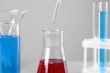 Gri arkaplanda pipetten mataraya sıvı damlatılıyor, yakın plan.