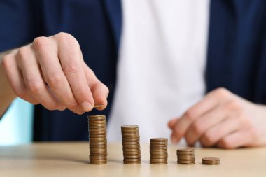 Finansal tasarruflar. Ahşap masaya para istifleyen adam, yakın plan.