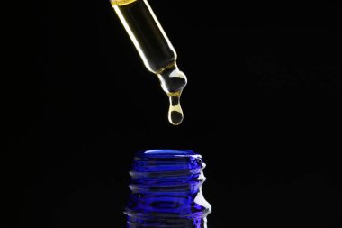 Siyah arka planda pipetten şişeye tentür damlatıyor, yakın plan.