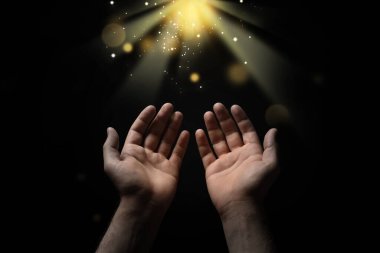 Hıristiyan adam karanlıkta kutsal ışığa doğru elini uzatıyor, yaklaş. Dua ve inanç.